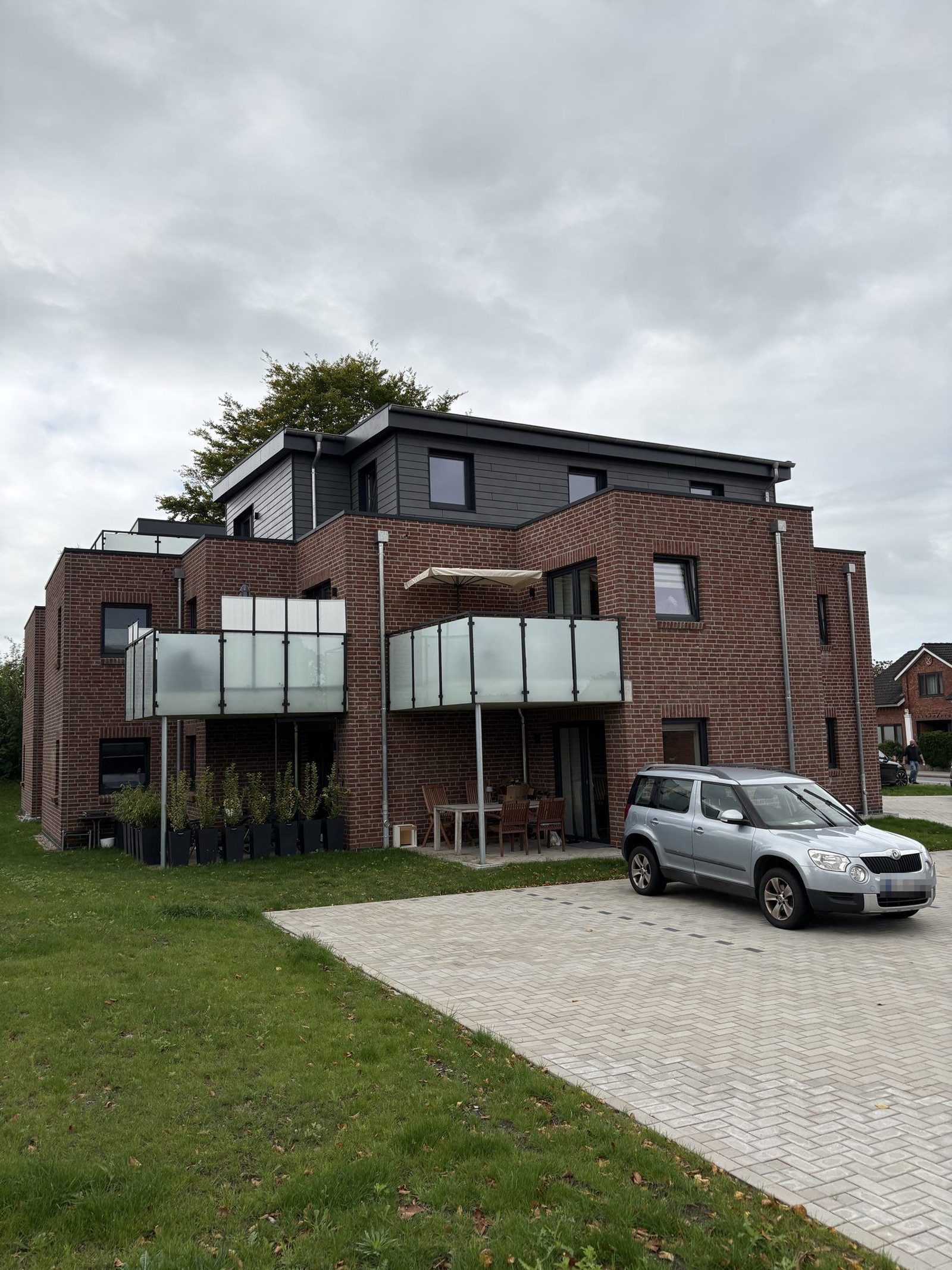 Das Mehrfamilienhaus von der Straßenseite, mit Zufahrt und Stellplätzen